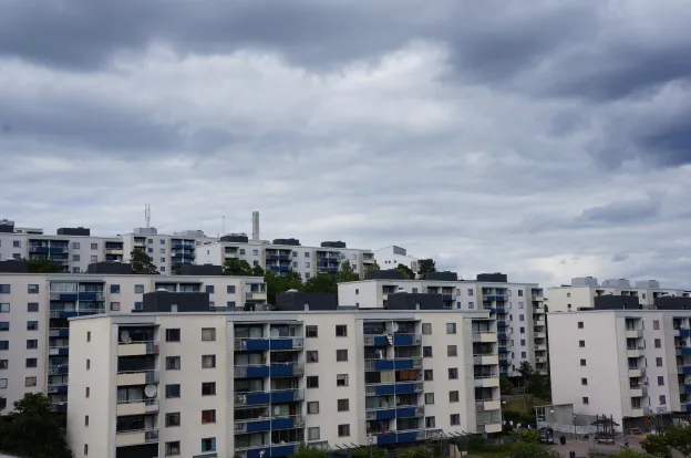 Rows of multi-story residential apartment buildings with balconies stretching toward a heavily clouded grey sky, muted white and dark-grey palette.